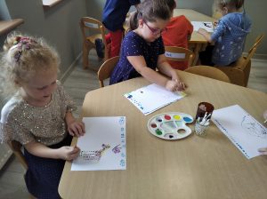 Bystrzaki -Dwie dziewczynki przy stoliku malują "kropkowy" obrazek na kartce za pomocą patyczków maczanych w farbie.