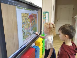 Bystrzaki - Dziewczynka i chłopiec stojąc przy tablicy interaktywnej i na dużym ekranie, łącząc punkty, grają w interaktywną grę "Połącz kropki". Na ekranie powoli powstaje obrazek, na którym widnieje grzyb.