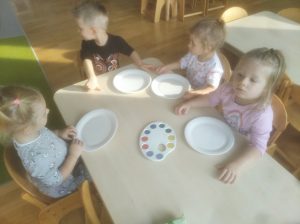 Krasnoludki - grupa dzieci siedzi przy stoliku i maluje farbami