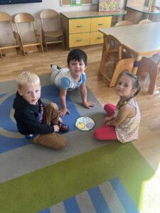 ZUCHY - Troje dzieci siedzi na dywanie z ułożoną układanką