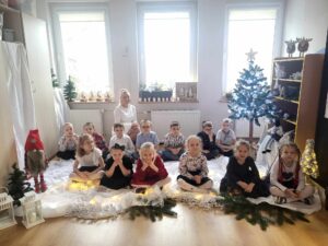 Dzieci wraz z panią siedzą, otoczone świąteczną dekoracją