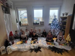 Dzieci siedzą, otoczone świąteczną dekoracją mając przed sobą instrumenty muzyczne